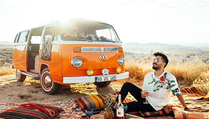 Ein Mann mit Sonnenbrille lächelt zufrieden und im Hintergrund ist sein neuerworbenes Auto zu sehen